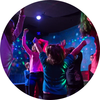 A group of kids dancing under colorful disco lights, raising their arms in excitement.