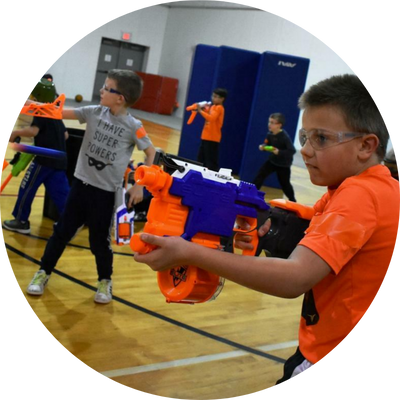 Kids playing with toy blasters in a gym, wearing safety goggles for protection.