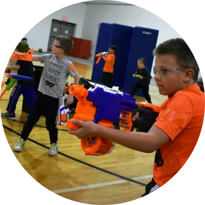 Kids playing with toy blasters in a gym, wearing safety goggles for protection.