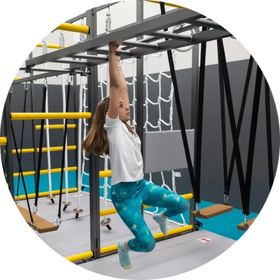 Child navigating a hanging obstacle course, swinging from a metal ladder in an indoor adventure setup.
