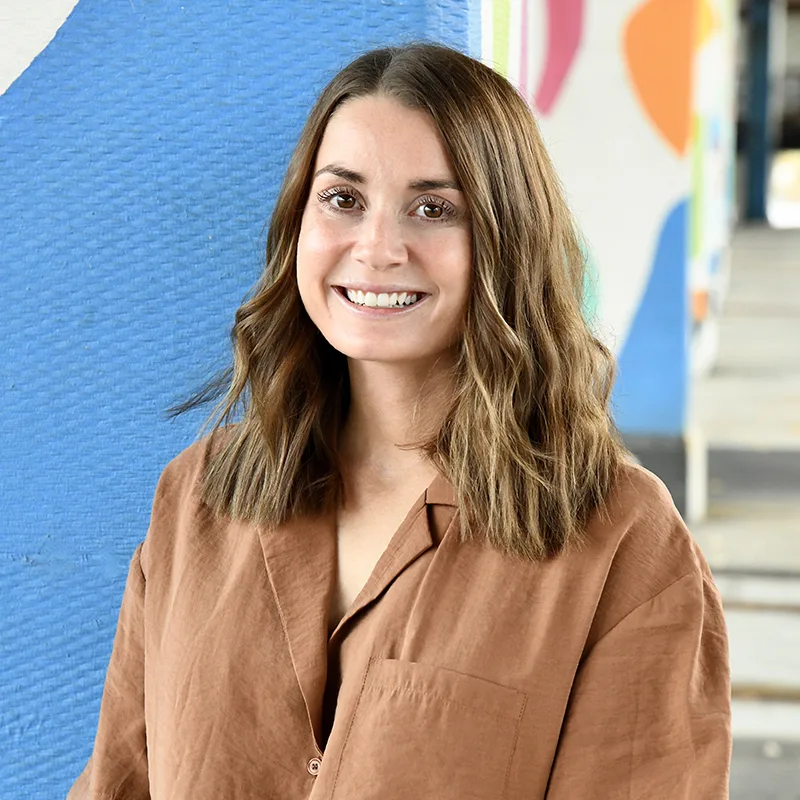 A woman smiling in front of a colorful mural background.