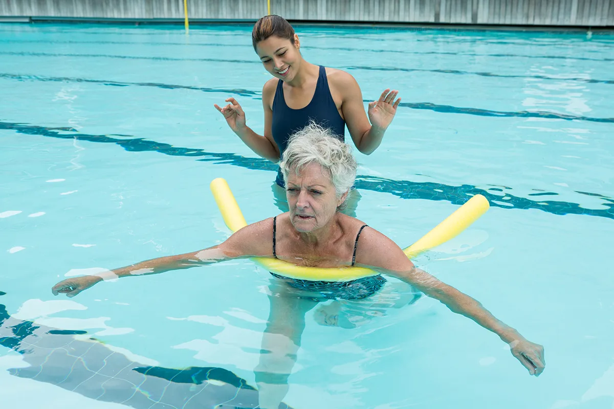 Instructor guiding a senior woman during a water exercise session in a pool.