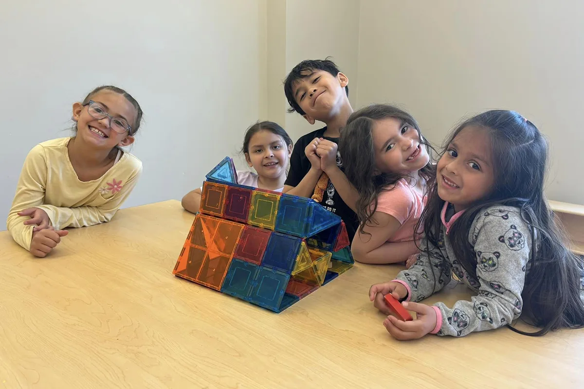 Children smiling and posing with a colorful magnetic tile structure on a table.