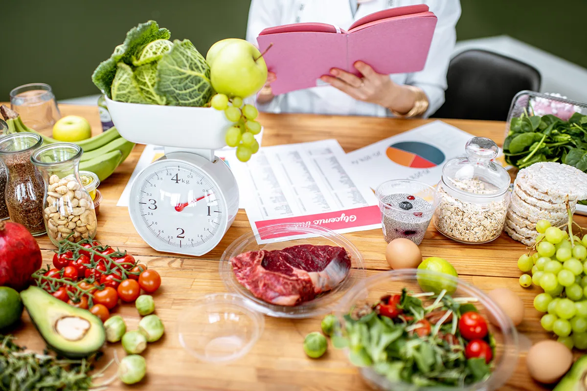 A table with fresh fruits, vegetables, grains, and a food scale, used for healthy meal planning and nutrition tracking.