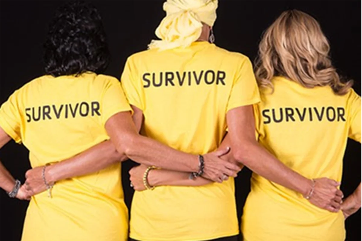 Three women wearing yellow "Survivor" shirts stand with their arms around each other, facing away.
