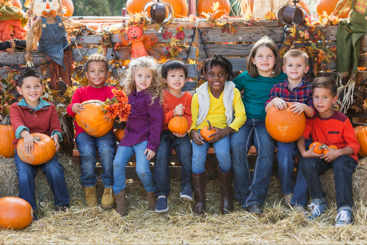 Group of kids at a fall festival posing for a photo holding pumpkins