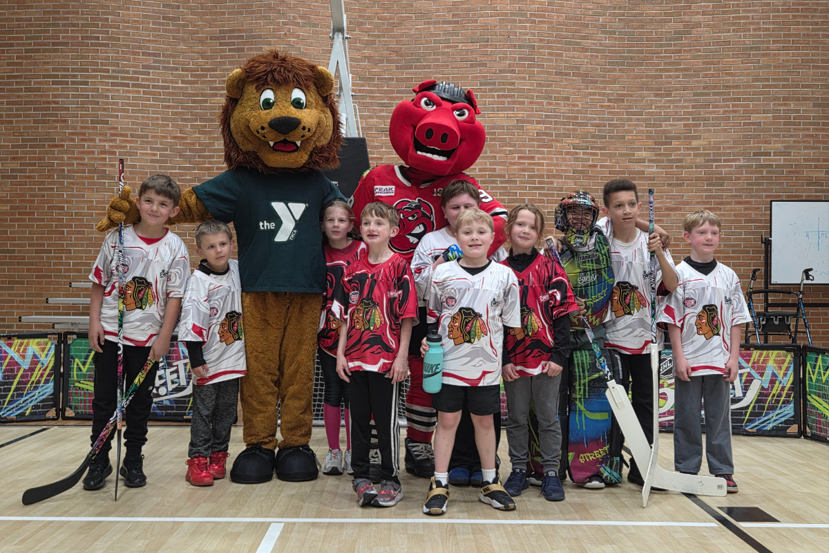 Group of kids in hockey gear posing for a photo with two mascots