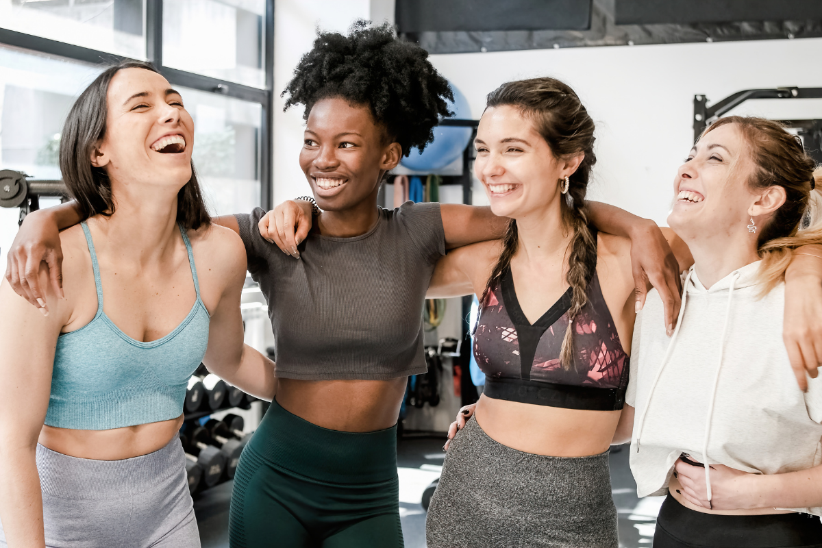 Four women at the gym standing in a circle smiling