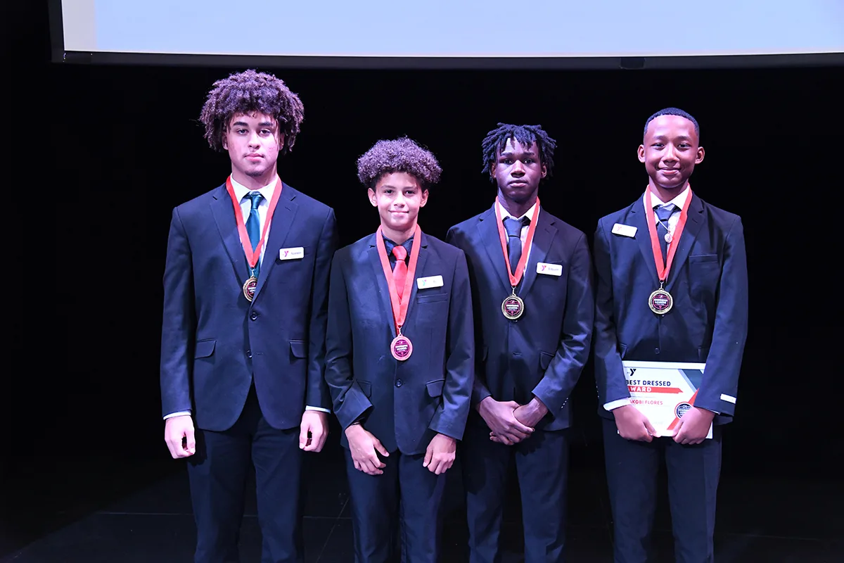 Four young men in suits with medals, posing on stage after receiving awards.