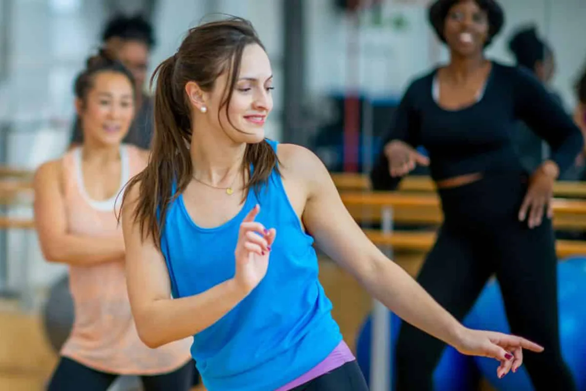 Women smiling and dancing in a fitness class setting.