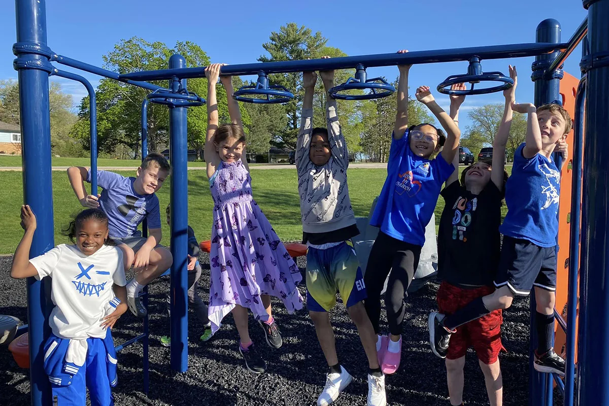 Kids hanging on playground equipment outside on a sunny day.