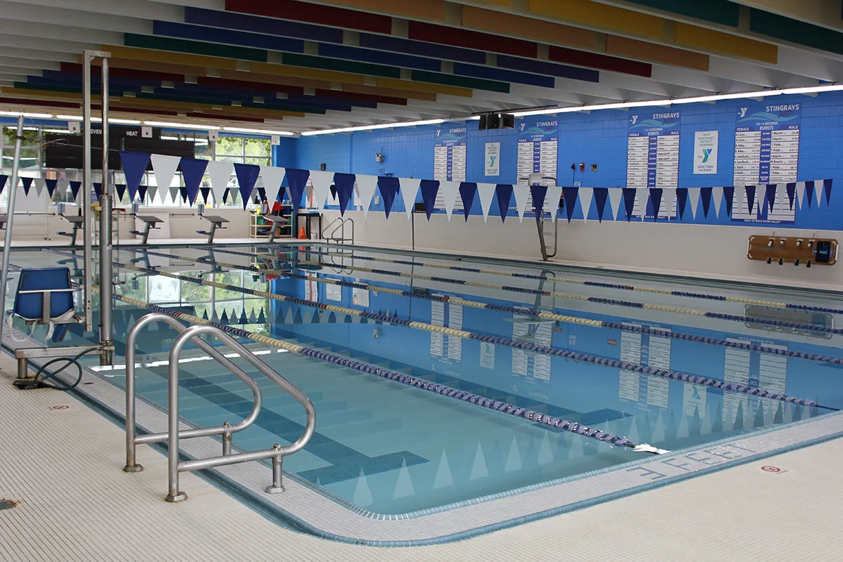 Bright indoor pool with blue-and-white lane markers and flags, ready for swim practice or recreational use.