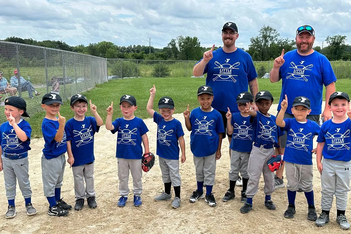 Group of young Little Sluggers baseball players and coaches celebrating on the field.