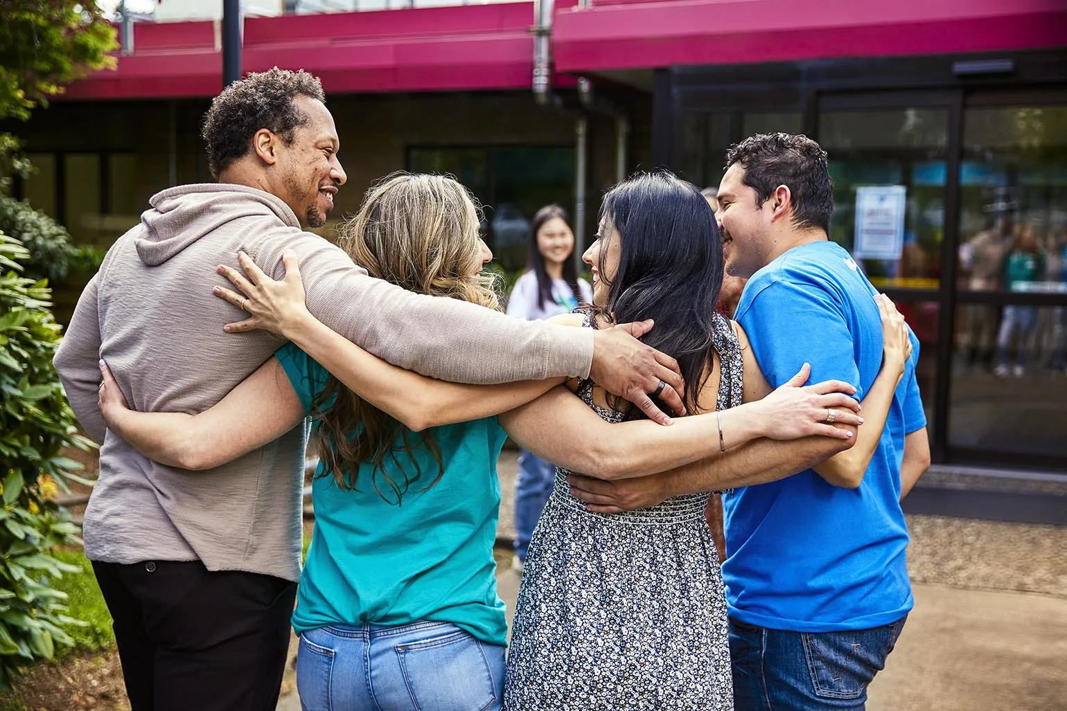 Group of adults standing outside in a close embrace, smiling and enjoying a moment together.