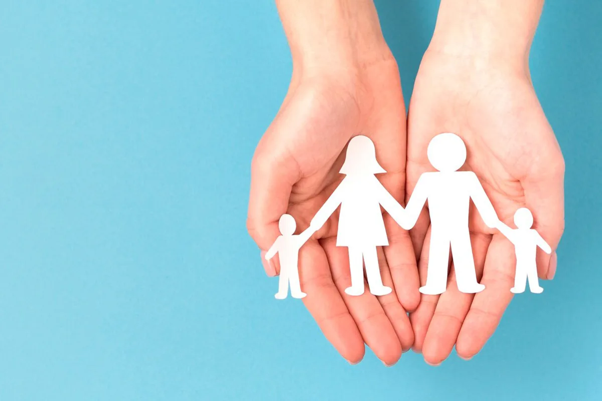 Hands holding paper cutout of a family of four, symbolizing family care and support.