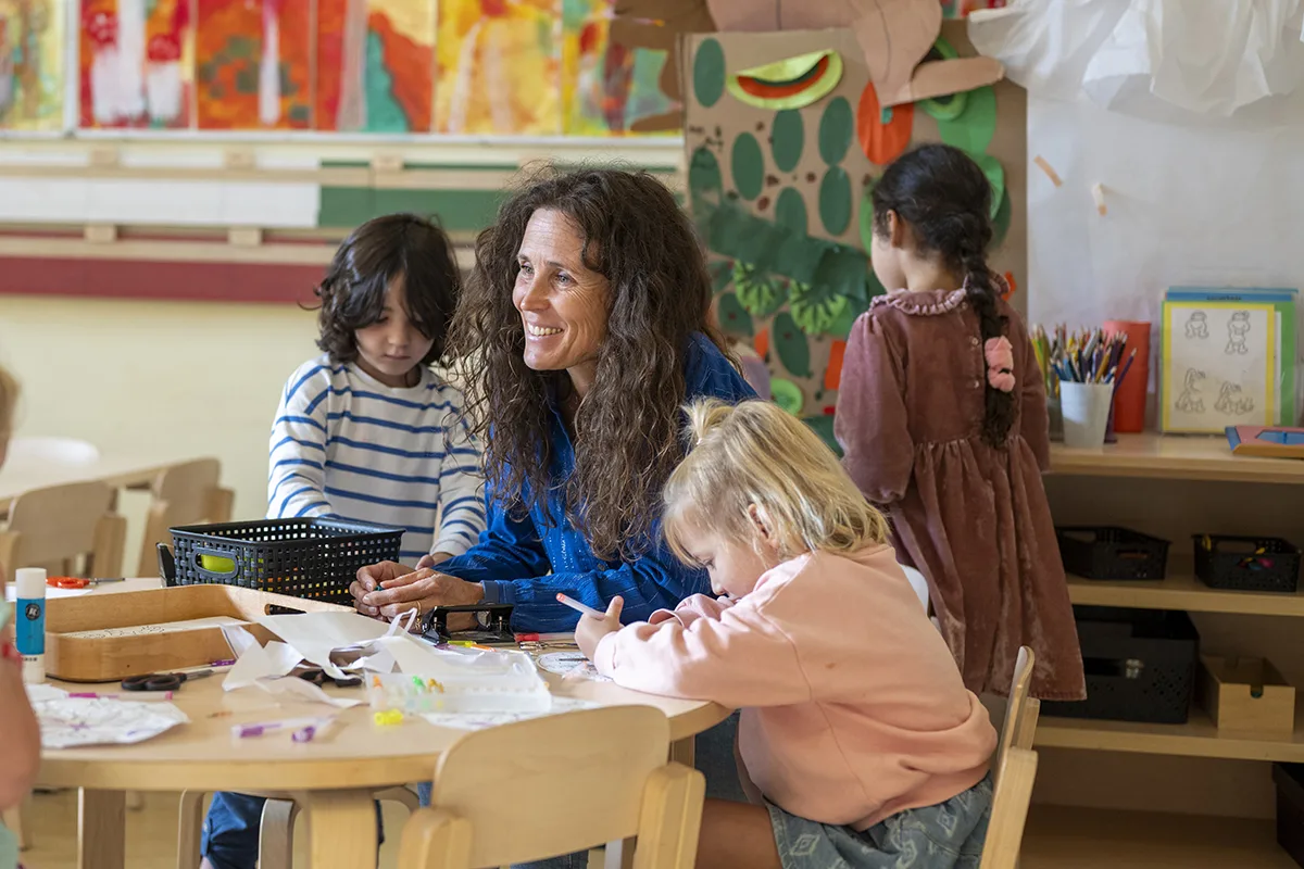 Teacher helping young children with crafts, classroom setting.