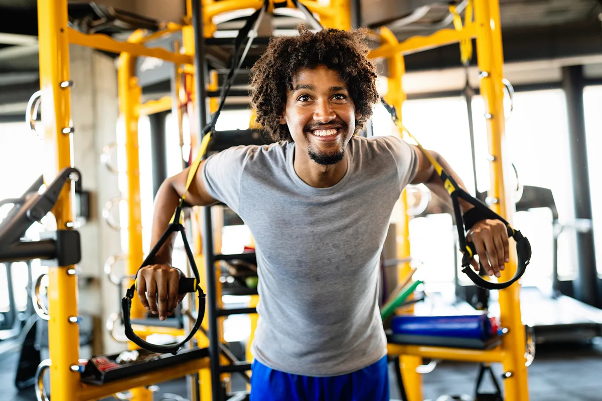 Man working out with suspension straps, smiling in gym setting.