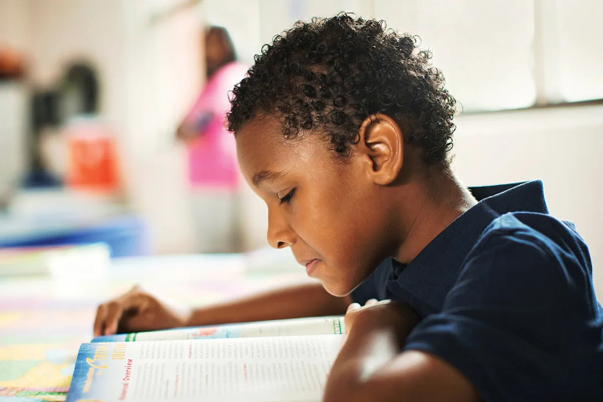 Young boy focused on reading a book in classroom.