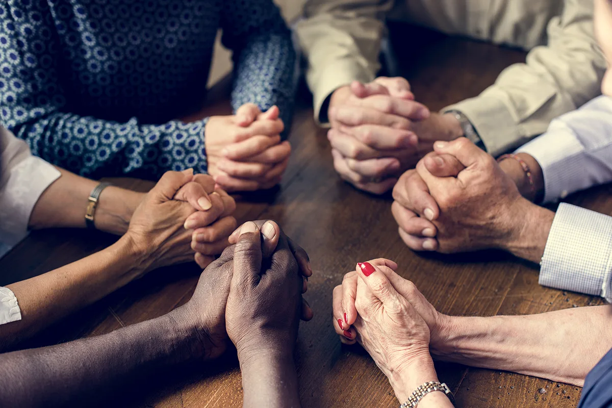 Group of diverse hands clasped together in unity around a wooden table.